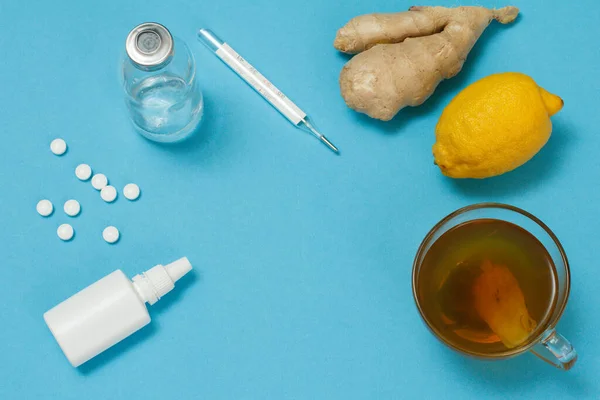 Nasal spray, pills, a glass bottlle, a mercury thermometer, cup of tea, lemon and ginger. Top view. Treatment kit concept. Health remedy foods for cold and flu relief.