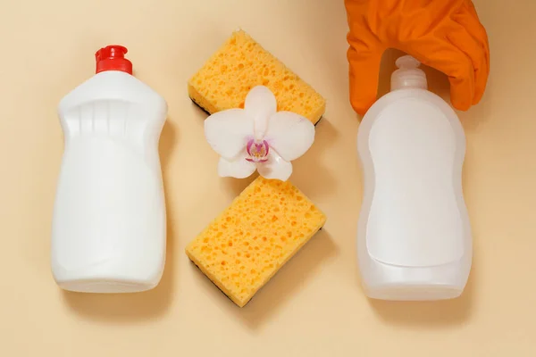 Plastic bottles of dishwashing liquid, detergent for microwave ovens and stoves with a hand in a rubber glove, sponges and a white orchid flower. Top view. Washing and cleaning set.