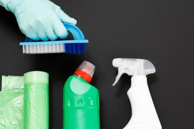 Siyah arka planda fırça, çamaşır ve temizlik seti olan koruyucu eldivenli bir kadın eli. Üst görünüm.