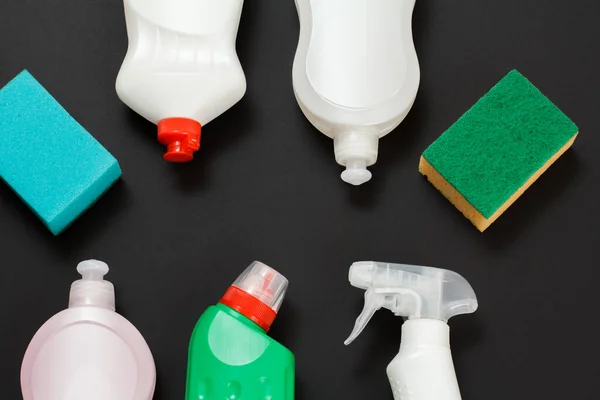 Plastic bottles of washing liquid and sponges on the black background. Top view. Washing and cleaning set.