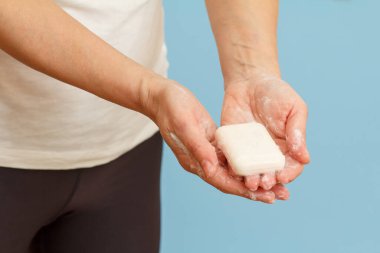 Mavi arka planda ellerini sabunla yıkayan bir kadın. Doğru şekilde ellerini temizlemek enfeksiyona karşı korur. Hijyen ve temizlik kavramı.