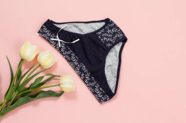 Pembe arka planda lale çiçekleri olan siyah pamuklu külotlar. Kadın iç çamaşırı seti. Üst görünüm.