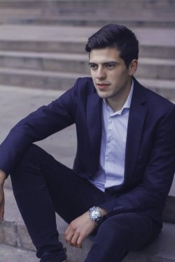 Tarz saçlı yakışıklı genç adam. Adam belgili tanımlık merdiven üstünde oturuyor. 