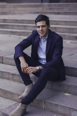 Tarz saçlı yakışıklı genç adam. Adam belgili tanımlık merdiven üstünde oturuyor. 