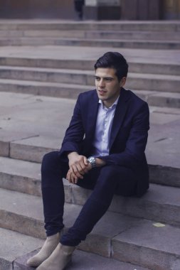 Tarz saçlı yakışıklı genç adam. Adam belgili tanımlık merdiven üstünde oturuyor. 