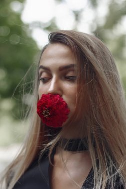 Zarif kadın ile onun ağzına bir çiçek. Çiçek kırmızı. Kız harika görünüyor. Uzun güzel saç.