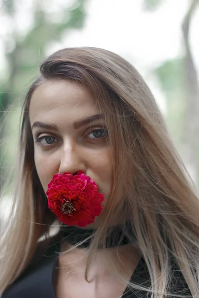 Elegant kvinna med en blomma i hennes mun. Blomma röd. Flickan ser fantastisk. Långa vackra hår. — Stockfoto