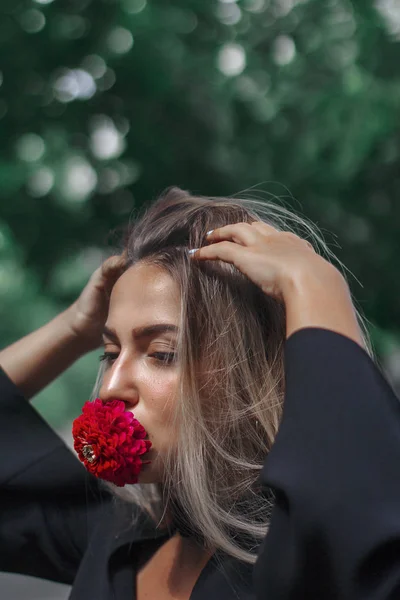 Mujer elegante con una flor en la boca. Flor roja. La chica se ve increíble. Cabello largo hermoso . — Foto de Stock