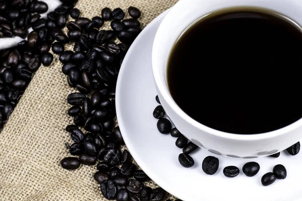Beyaz Kupası ve kahve çekirdeği kumaş ve ahşap arka plan üzerinde siyah kahve.