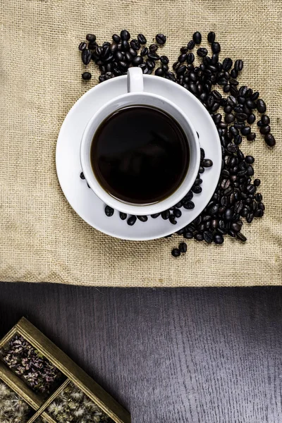 Beyaz Kupası ve kahve çekirdeği kumaş ve ahşap arka plan üzerinde siyah kahve.