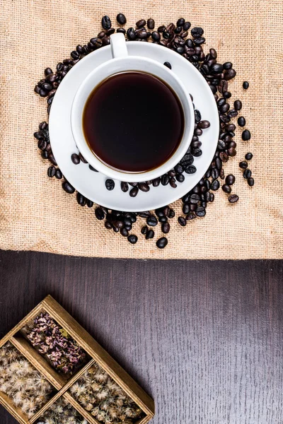 Beyaz Kupası ve kahve çekirdeği kumaş ve ahşap arka plan üzerinde siyah kahve.