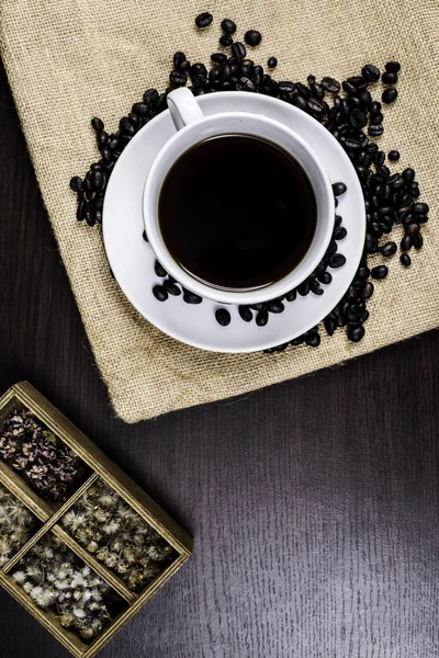 Beyaz Kupası ve kahve çekirdeği kumaş ve ahşap arka plan üzerinde siyah kahve.