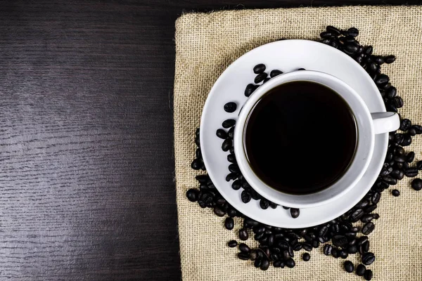 Beyaz Kupası ve kahve çekirdeği kumaş ve ahşap arka plan üzerinde siyah kahve.