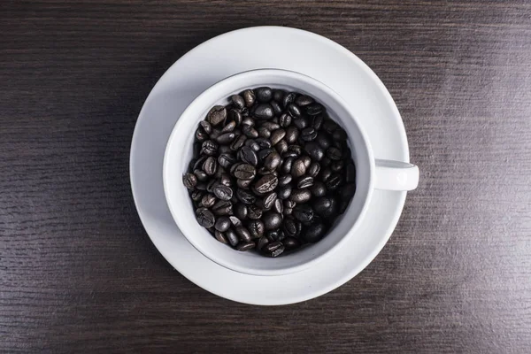 ahşap arka plan üzerinde beyaz fincan kahve çekirdeği.
