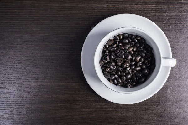 ahşap arka plan üzerinde beyaz fincan kahve çekirdeği.