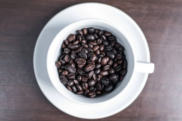 ahşap arka plan üzerinde beyaz fincan kahve çekirdeği.