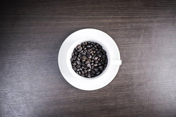 ahşap arka plan üzerinde beyaz fincan kahve çekirdeği.