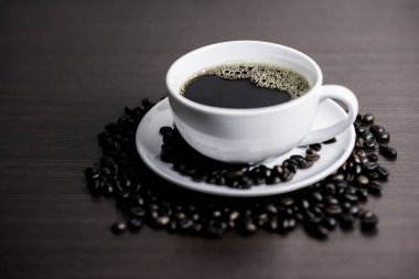 Beyaz Kupası ve kahve çekirdeği ahşap arka plan üzerinde siyah kahve.