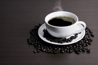 Beyaz Kupası ve kahve çekirdeği ahşap arka plan üzerinde siyah kahve.