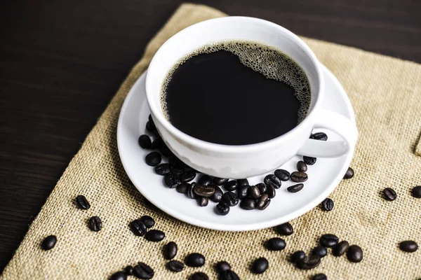 Beyaz Kupası ve kahve çekirdeği ahşap masa arka plan üzerinde siyah kahve.