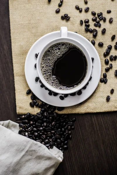 Beyaz Kupası ve kahve çekirdeği ahşap masa arka plan üzerinde siyah kahve.