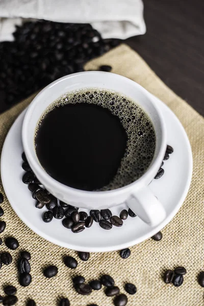 Beyaz Kupası ve kahve çekirdeği ahşap arka plan üzerinde siyah kahve.
