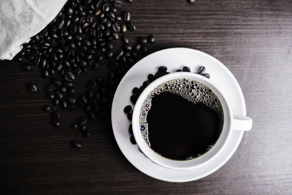 Beyaz Kupası ve kahve çekirdeği ahşap arka plan üzerinde siyah kahve.