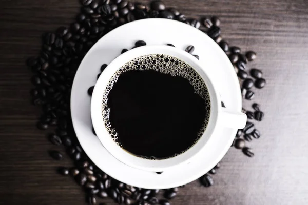 Beyaz Kupası ve kahve çekirdeği ahşap arka plan üzerinde siyah kahve.