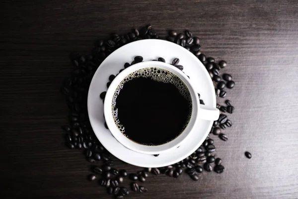 Beyaz Kupası ve kahve çekirdeği ahşap arka plan üzerinde siyah kahve.