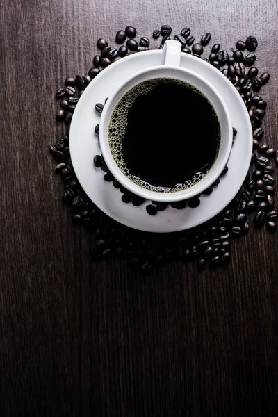 Beyaz Kupası ve kahve çekirdeği ahşap arka plan üzerinde siyah kahve.