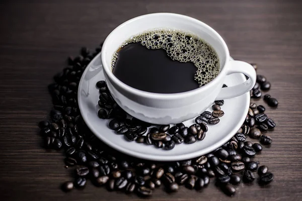 Beyaz Kupası ve kahve çekirdeği ahşap arka plan üzerinde siyah kahve.