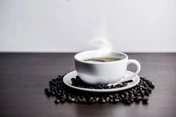 Beyaz Kupası ve kahve çekirdeği ahşap arka plan üzerinde siyah kahve.