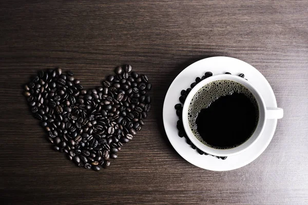 Beyaz Kupası ve kahve çekirdeği ahşap arka plan üzerinde siyah kahve.