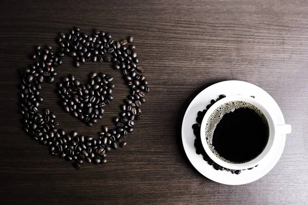 Beyaz Kupası ve kahve çekirdeği ahşap arka plan üzerinde siyah kahve.