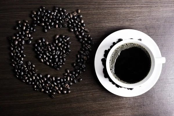 Beyaz Kupası ve kahve çekirdeği ahşap arka plan üzerinde siyah kahve.