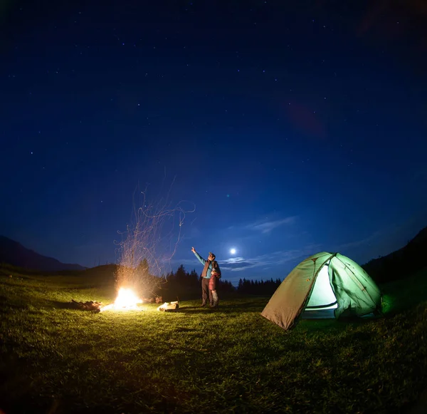 Father and son near campfire and tent under night sky