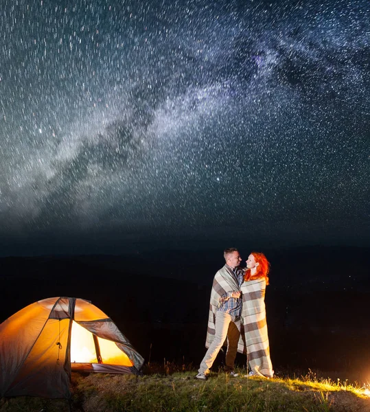 Sweety couple hikers standing together near campfire and tent at night and enjoying starry sky. Pair covered with a plaid. Amazing Milky way — Stock Photo, Image