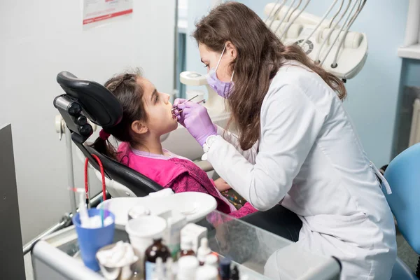 Young female doctor is treating patient girl teeth at dental clinic office. — Stock Photo, Image