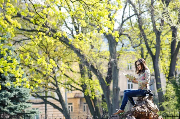 Девушка сидит в парке и читает карту — стоковое фото