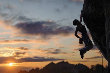 Silhouette of athletic woman climbing steep rock wall clipart