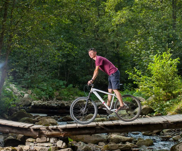 Adam ahşap köprü üzerinden bir bisiklet ile bir nehir üzerinde gidiyor — Stok fotoğraf