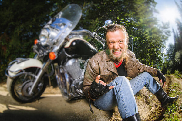 Male biker sitting on dirt road near motorcycle