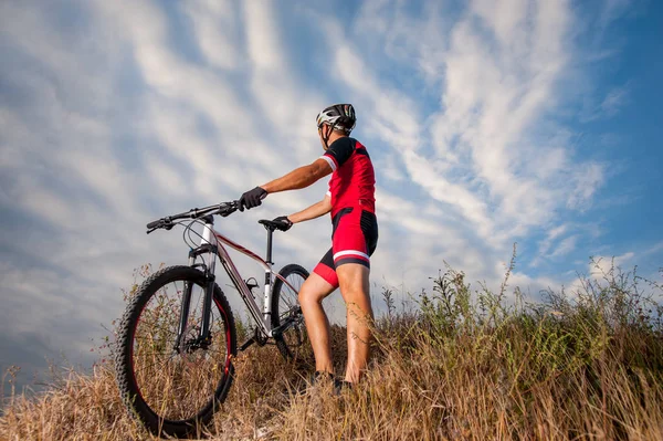 Mountainbiker rastet mit Fahrrad gegen blauen Himmel aus — Stockfoto