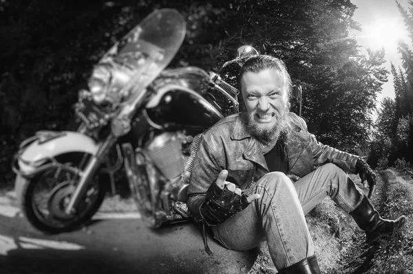 unshaven male biker sitting on dirt road near motorcycle