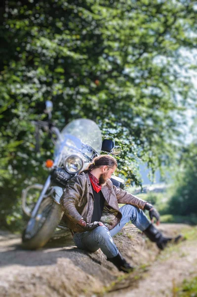 Male biker sitting on dirt road near motorcycle — Stock Photo, Image