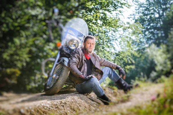 オートバイの近くの未舗装の道路上に座っている男性のバイカー — ストック写真