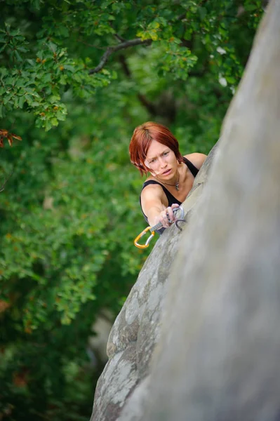 Athletic woman climbing steep cliff wall in summer time