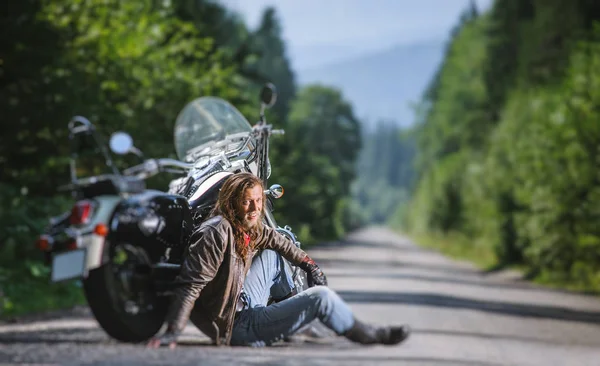 Masculino motociclista sentado na estrada perto da motocicleta — Fotografia de Stock