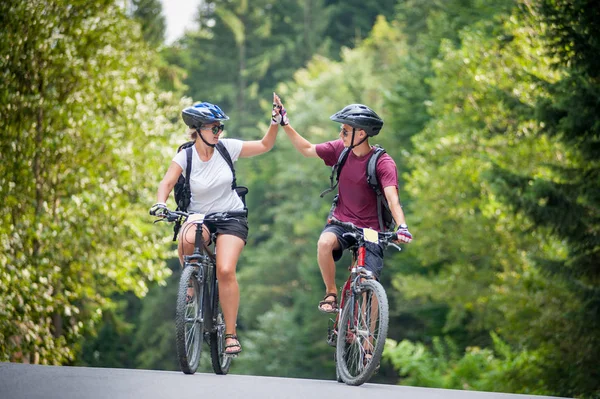 Счастливая пара едет по горной асфальтовой дороге на велосипедах — стоковое фото