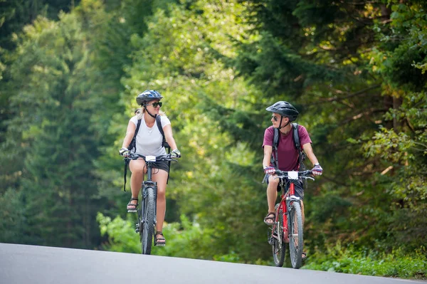 Счастливая пара едет по горной асфальтовой дороге на велосипедах — стоковое фото